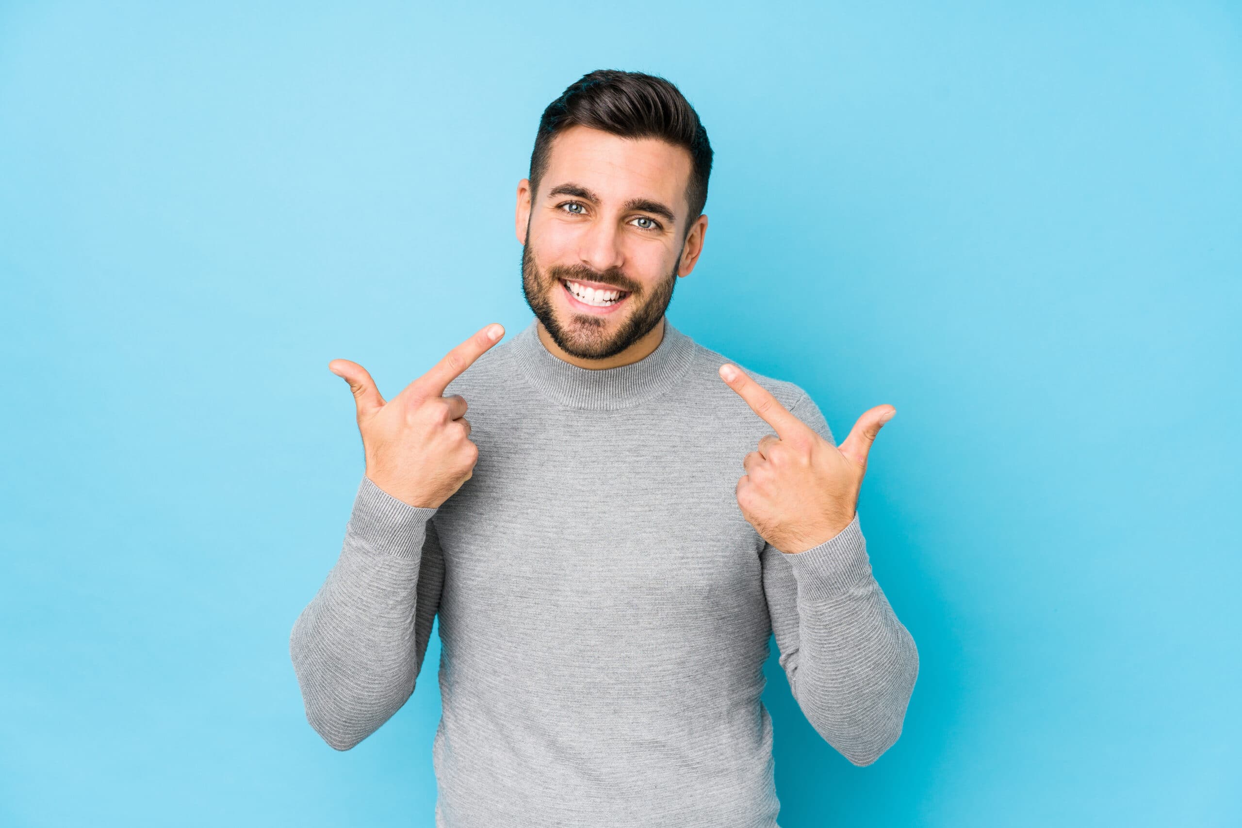 Young caucasian man against a blue background isolated smiles, pointing fingers at mouth.